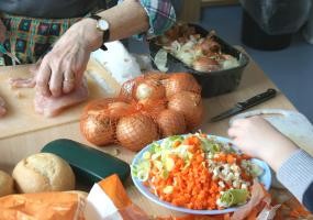 Kinderhand und Erwachsenenhand beim Schneiden von Gemüse und Fleisch